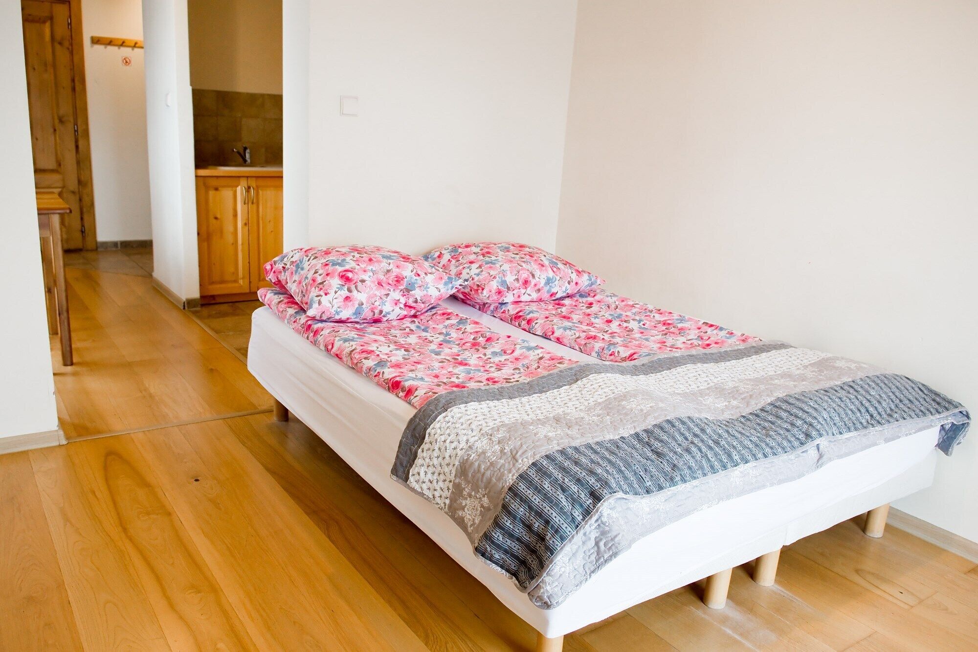 A single bed with floral bedding and a grey knitted throw, wooden flooring, and a wooden cabinet in the background.