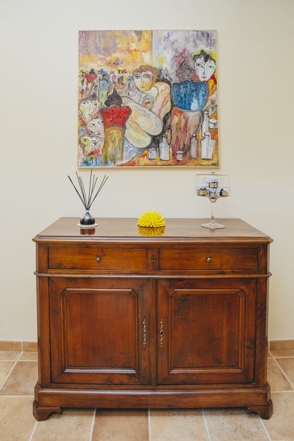 Un meuble en bois doté de deux tiroirs et d’un plateau en verre, placé contre un mur, avec une peinture abstraite aux couleurs vives accrochée au-dessus.