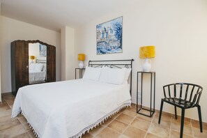 Une chambre d’hôtel avec un grand lit, une armoire en bois, un tableau représentant un paysage urbain, deux lampes de chevet et une chaise.