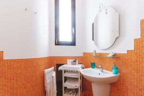 Une salle de bain avec des carreaux de mosaïque orange, un lavabo blanc, un miroir et une fenêtre.