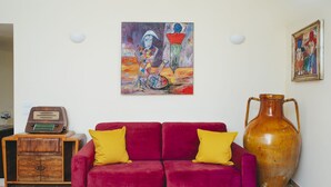 A living room with a red sofa, two yellow cushions, a wooden radio, a large vase, and two paintings on the wall. - Conte Orsini Apartment (Conversano)