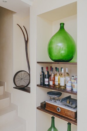 Un escalier avec une étagère fixée au mur, sur laquelle sont disposées différentes bouteilles, et un grand vase vert.