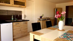 A modern kitchen with wooden cabinets, a built-in sink, and a dining area with a table set for two. - La Rosepierre, studio with a breathtaking view of the red-blue-green Salagou mountains (Liausson)