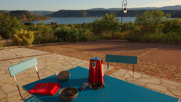 An outdoor seating area with a table, chairs, a kettle, and a view of a lake and hills. - La Rosepierre, studio with a breathtaking view of the red-blue-green Salagou mountains (Liausson)