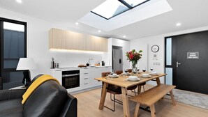A modern kitchen with a skylight, a dining area with a wooden table and chairs, and a black door with a shoe removal sign.