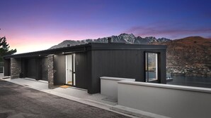 A modern building with a stone entrance, large windows, and a view of mountains and a lake.