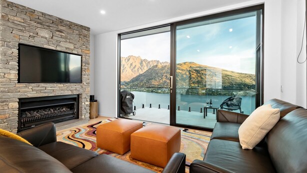A modern living room with a stone fireplace, leather sofas, a flat-screen TV, and a large sliding glass door offering a mountain view.