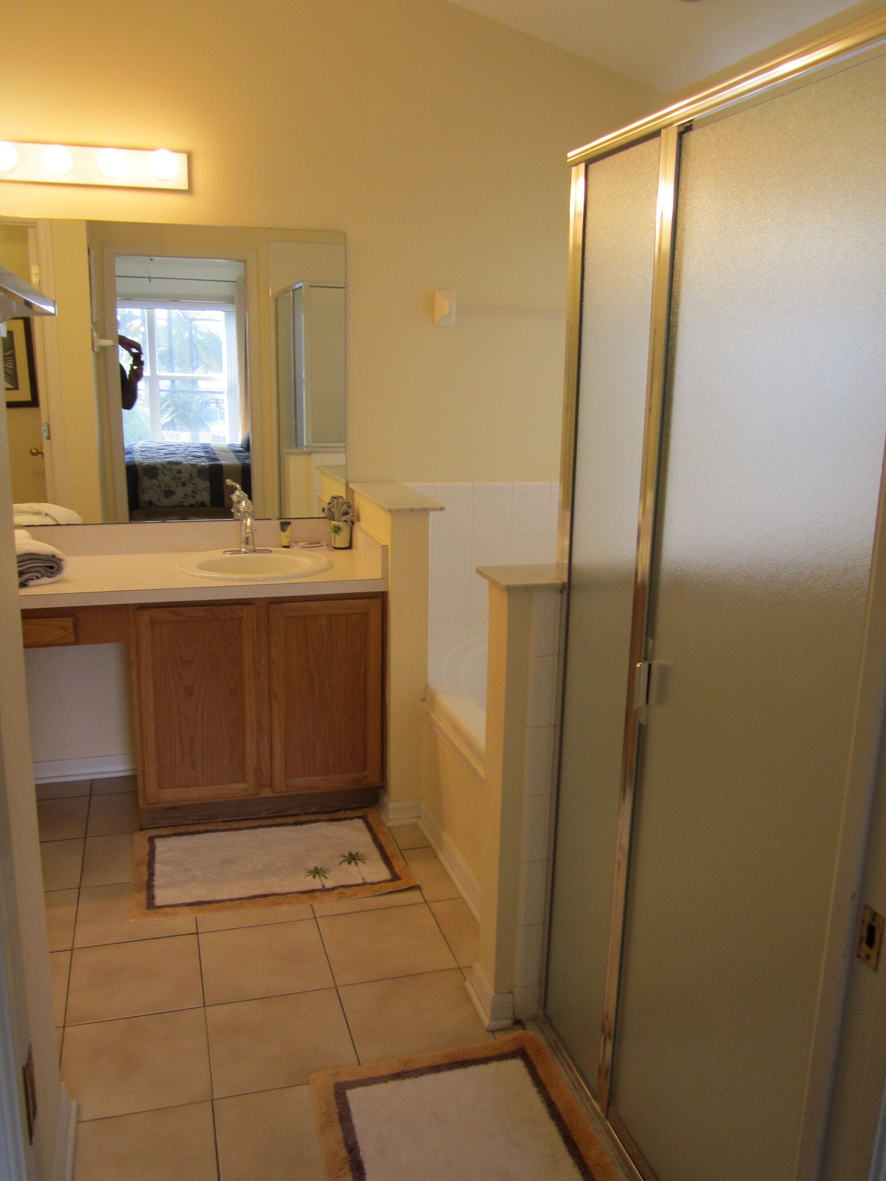 A bathroom with a wooden vanity, a sink, a mirror, and a shower area.