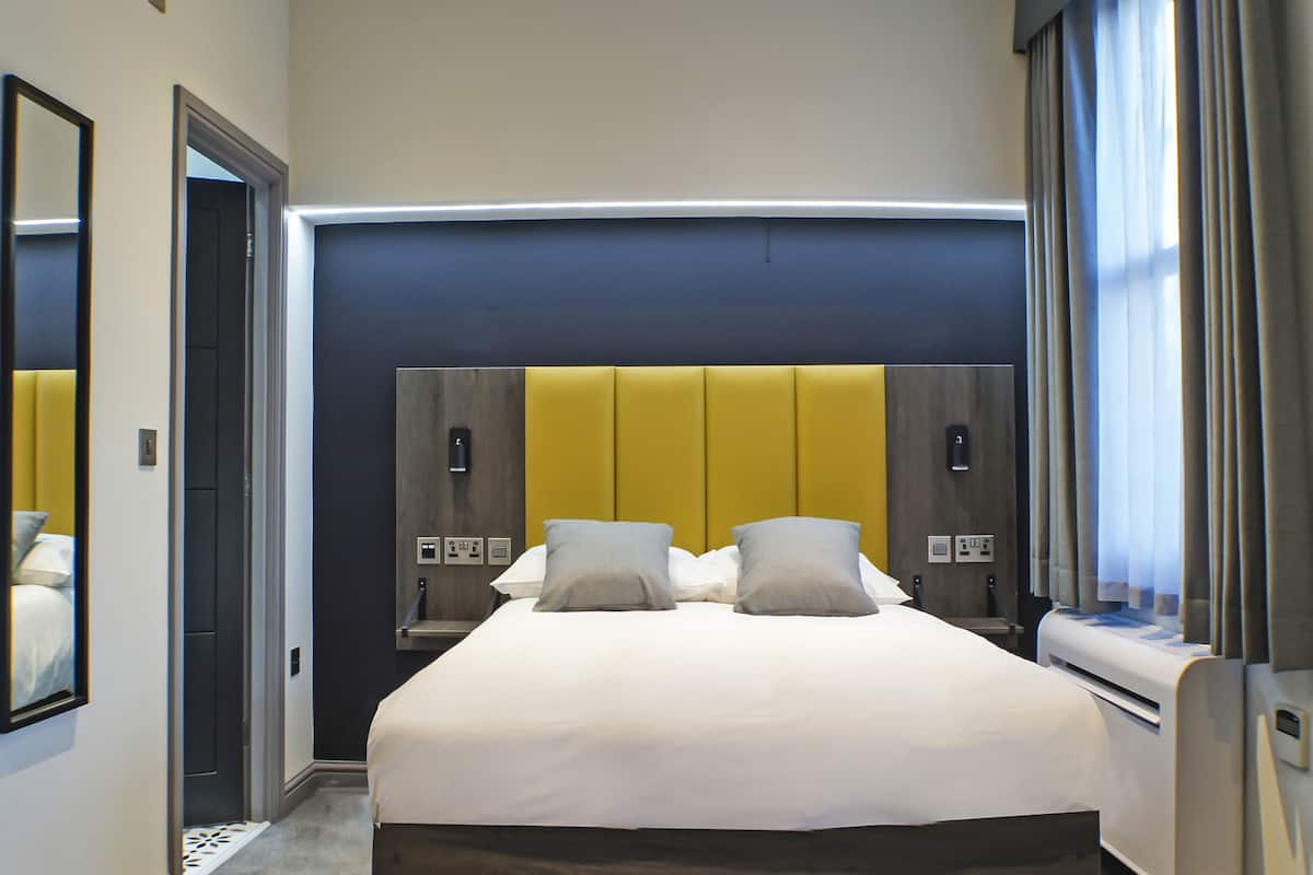 Ein Hotelzimmer mit einem großen Bett, zwei Nachttischen, einem Spiegel und einem Fenster mit Vorhängen.