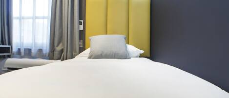 A hotel room with a large bed, a bedside table, and a window with curtains.