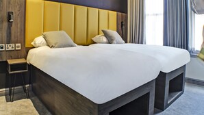 A modern hotel room with a large bed, a wooden nightstand, and a built-in bench at the foot of the bed. - OYO Tamworth Arms Boutique Pub & Hotel (Tamworth)