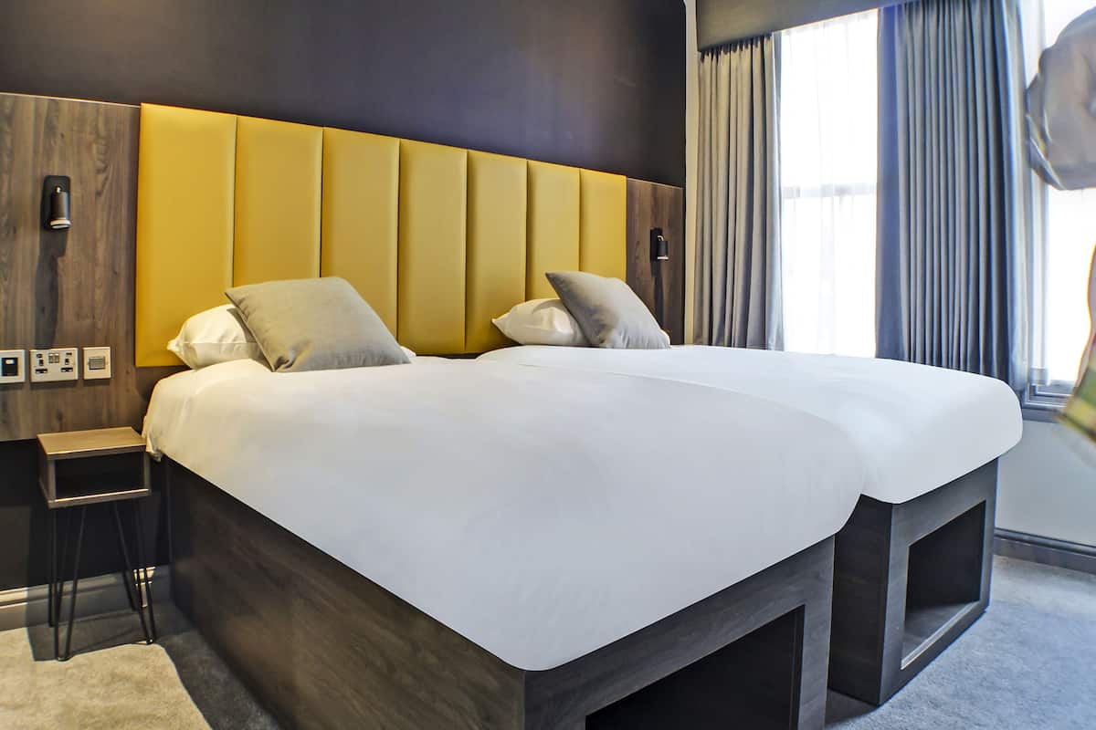 Ein modernes Hotelzimmer mit einem großen Bett, einem hölzernen Nachttisch und einer fest eingebauten Bank am Fußende des Bettes.