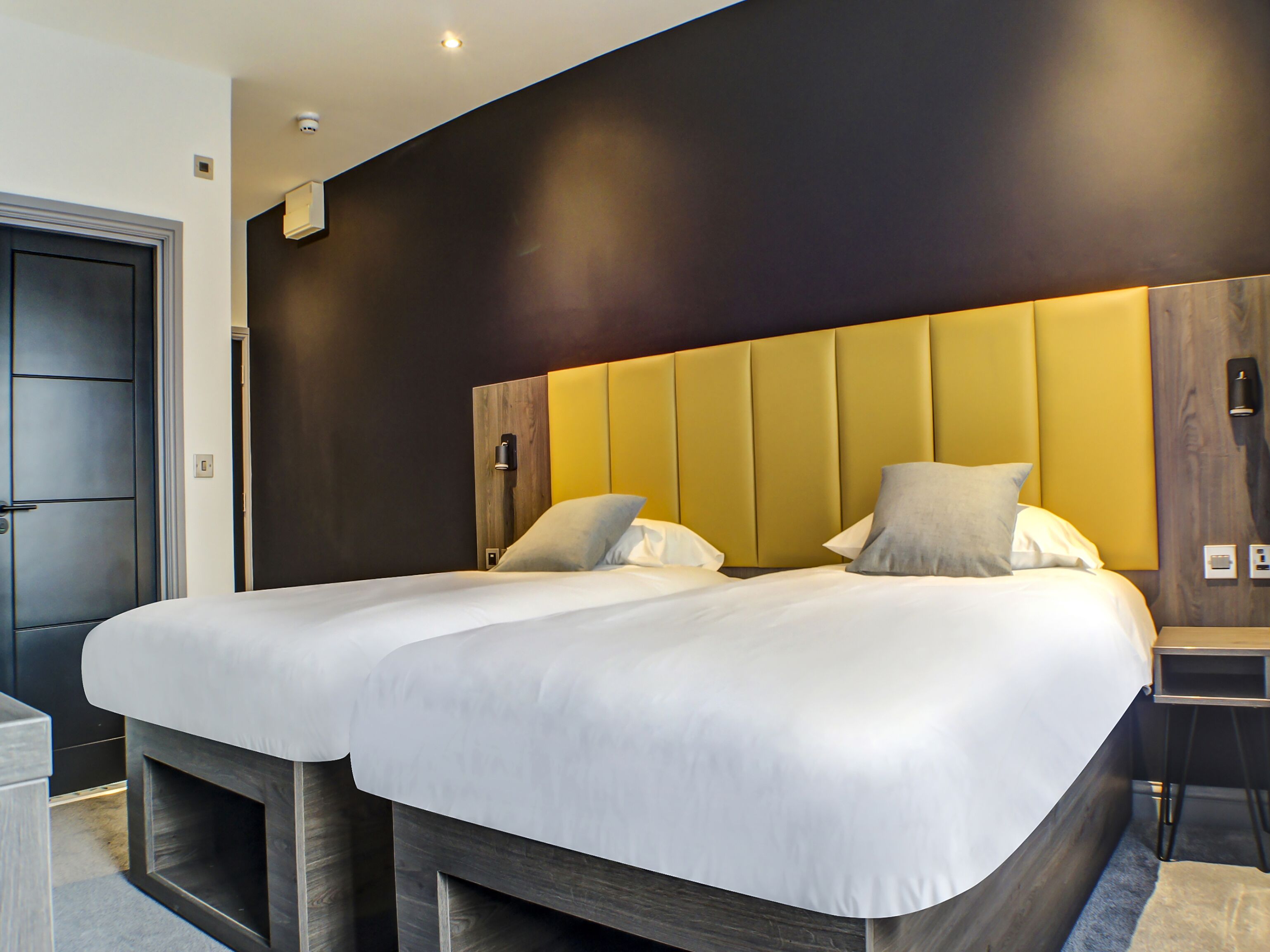 Une chambre d’hôtel avec un grand lit, une table de chevet et une tête de lit moderne.