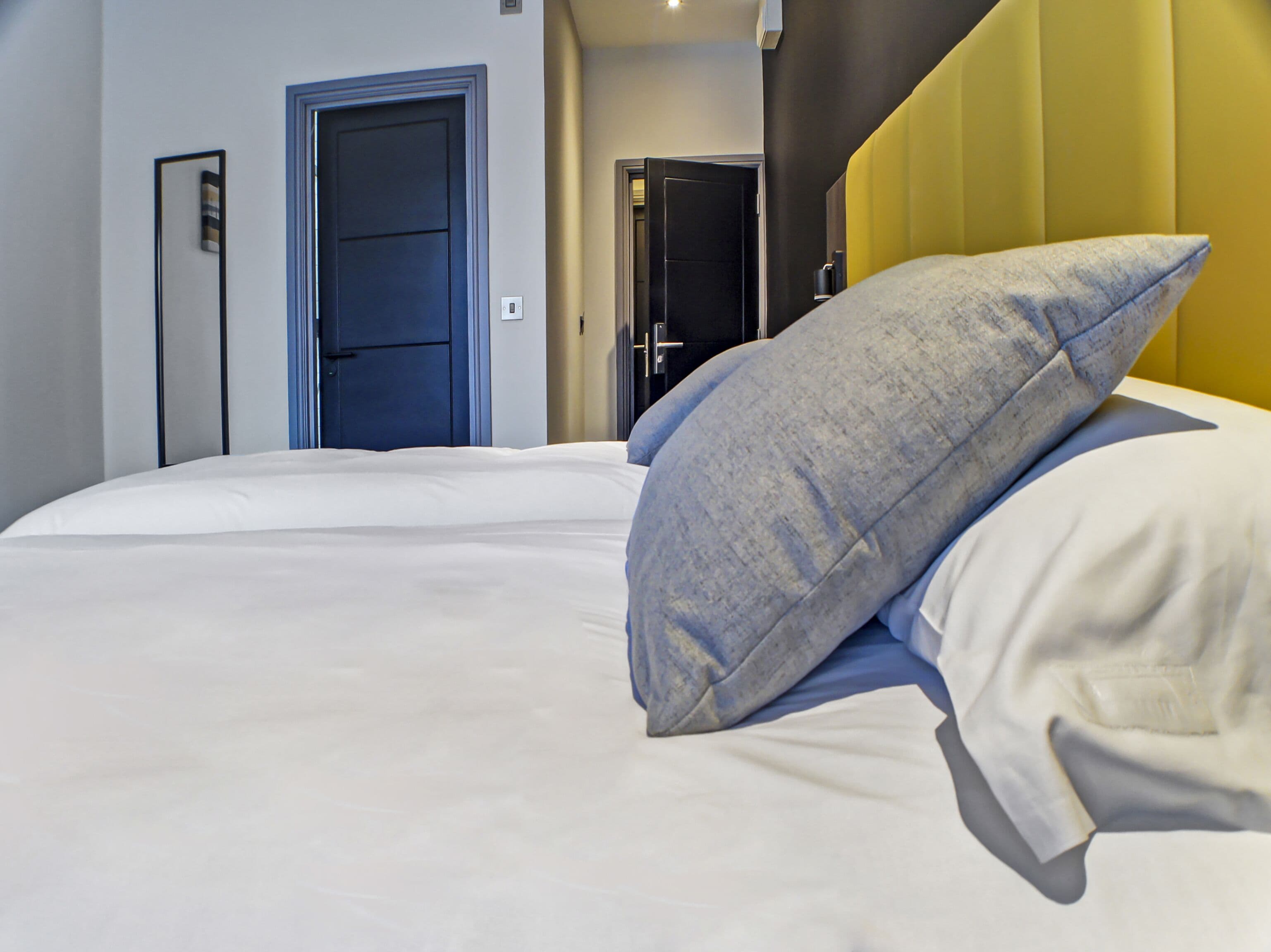 A hotel room with a large bed, two doors, and a yellow accent wall.