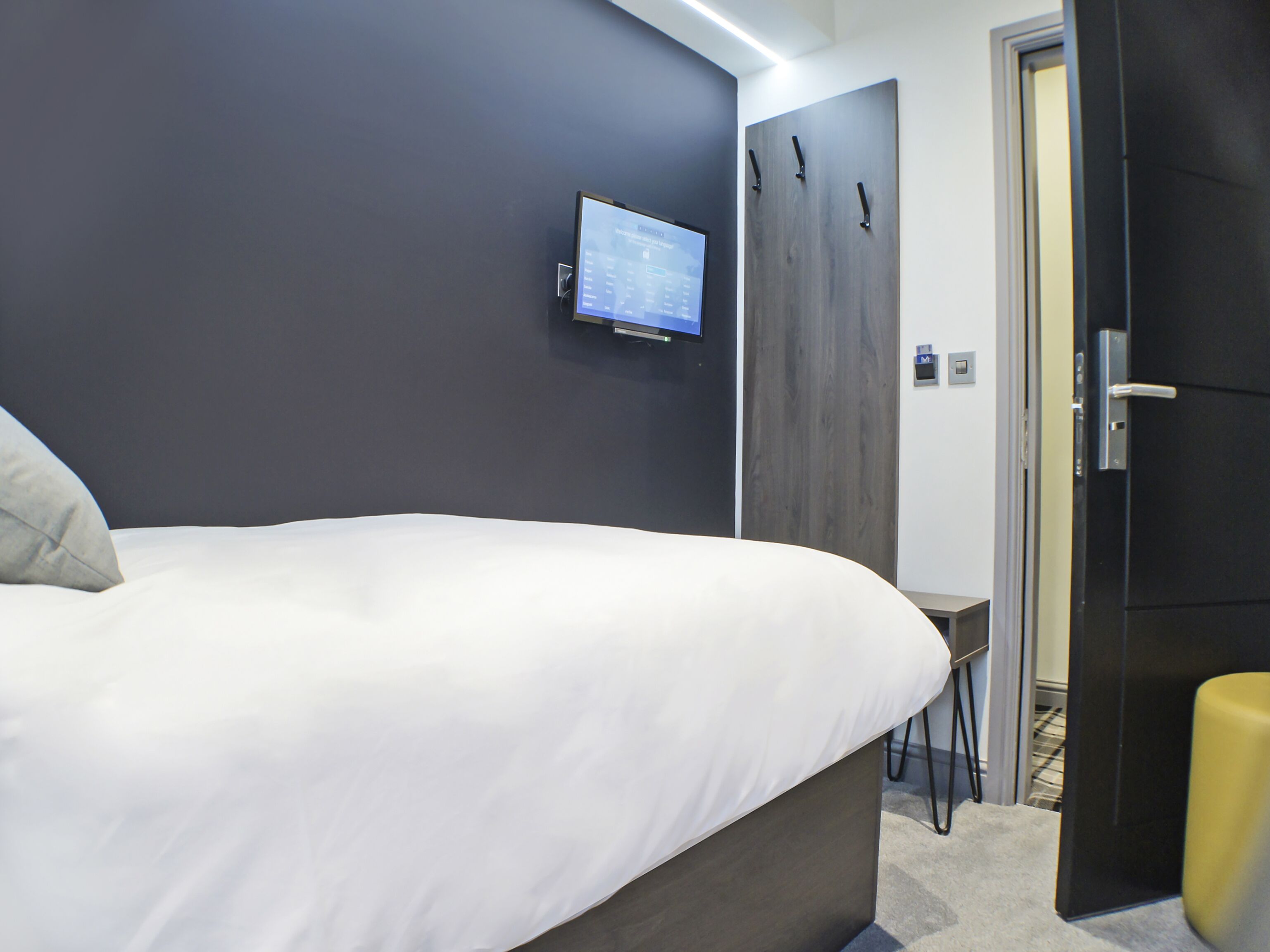 A modern bedroom with a bed, a TV mounted on the wall, and a wardrobe.
