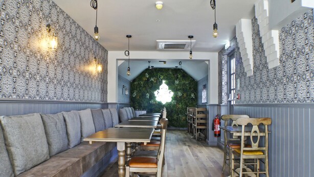 A restaurant interior with a long wooden bench seating area, a high ceiling with hanging lights, and a green wall feature. - OYO Tamworth Arms Boutique Pub & Hotel (Tamworth)