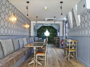 A restaurant interior with a long wooden bench seating area, a high ceiling with hanging lights, and a green wall feature. - OYO Tamworth Arms Boutique Pub & Hotel (Tamworth)