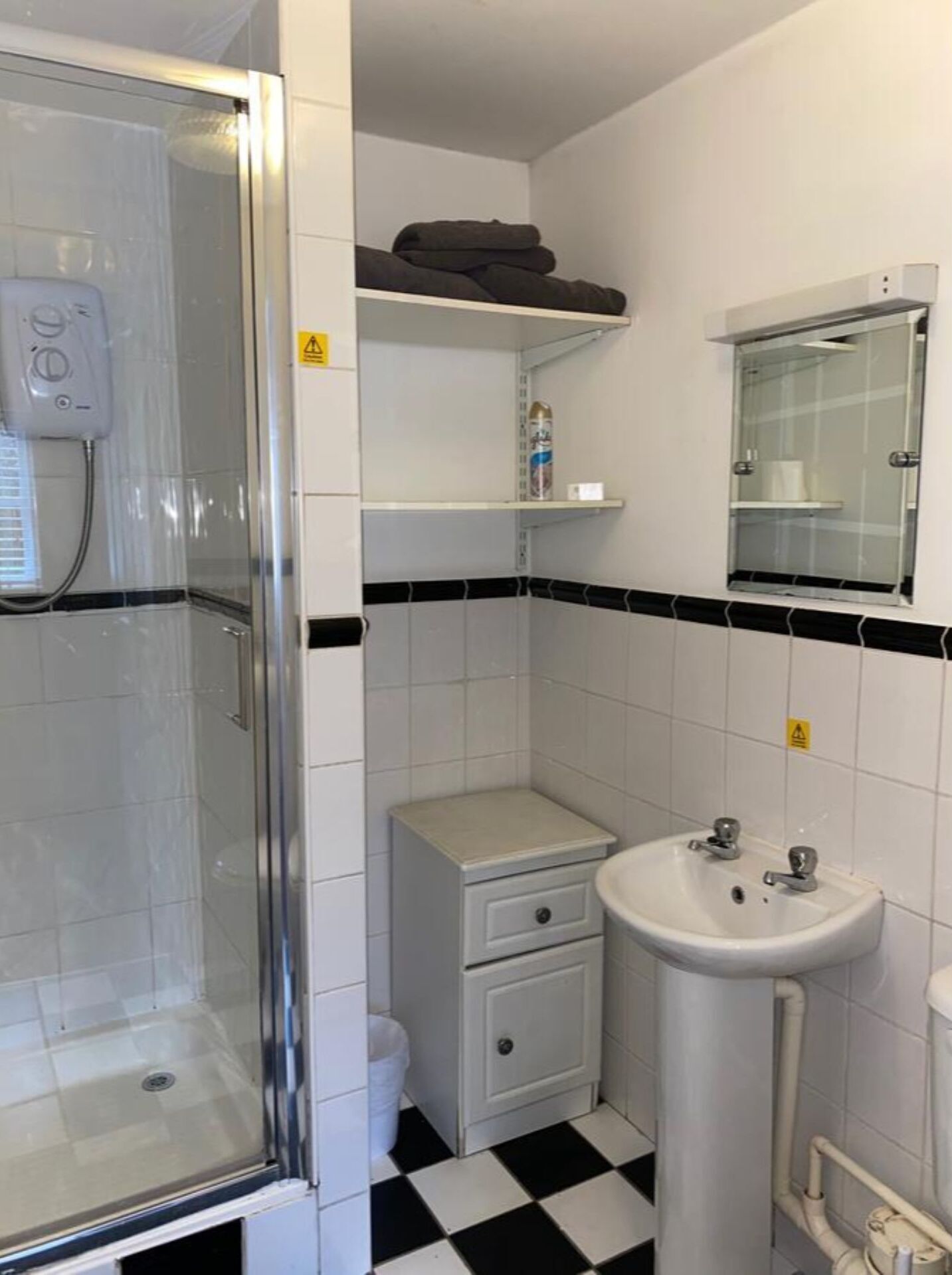 Une salle de bain avec une douche à parois de verre, un lavabo blanc, une petite table de chevet et un miroir.