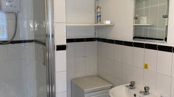 Une salle de bain avec une douche à parois de verre, un lavabo blanc, une petite table de chevet et un miroir.