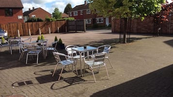 An outdoor patio area with metal tables and chairs, surrounded by brick walls and a wooden fence.