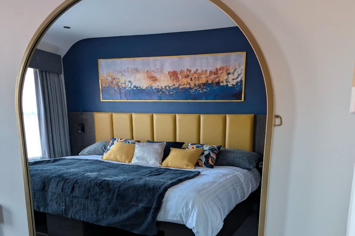 Ein Schlafzimmer mit einem großen Bett, einem Kopfteil, einem Bild an der Wand und einem Spiegel.