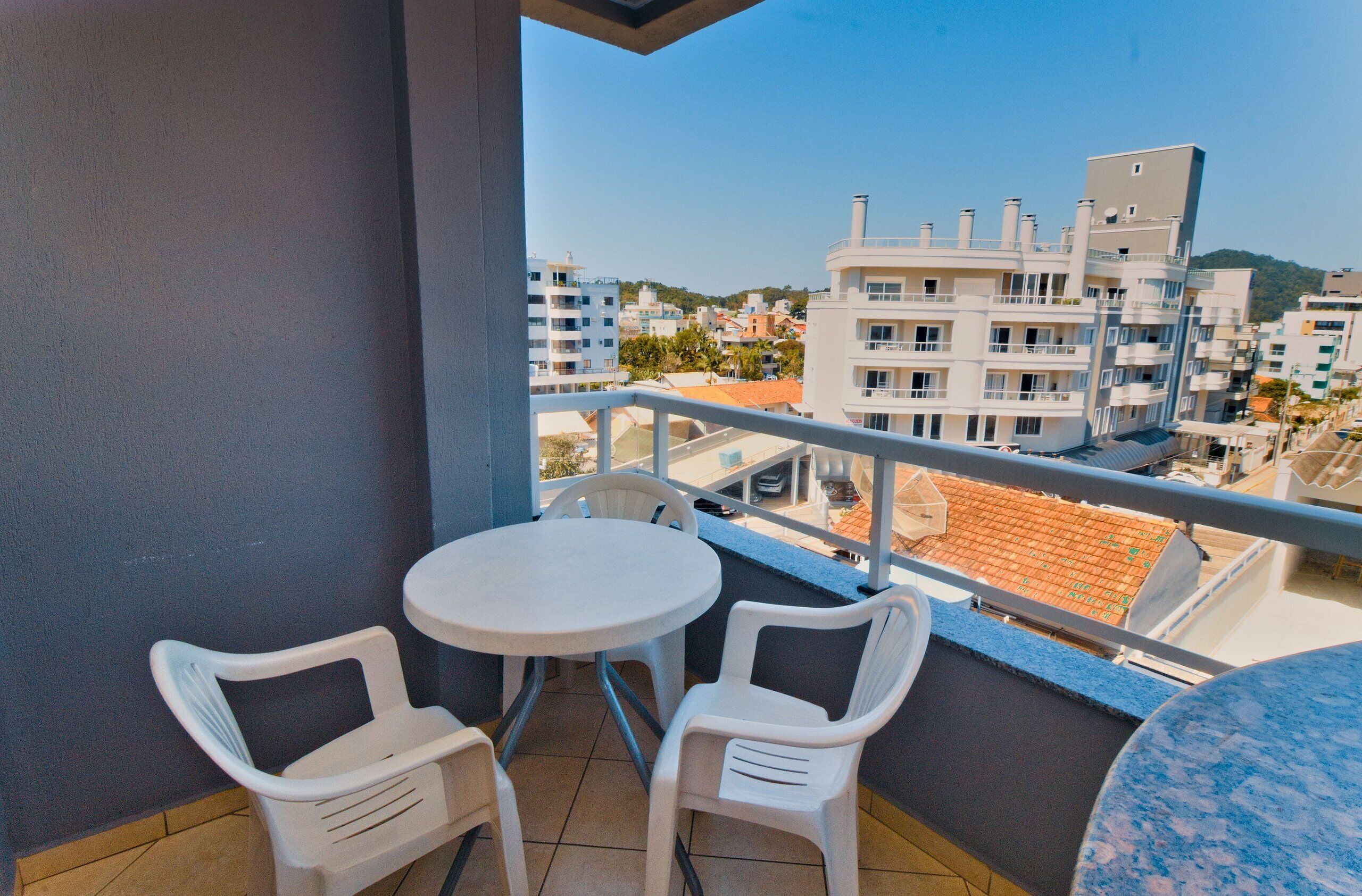 Un balcon avec deux chaises en plastique blanc et une petite table ronde, d’où l’on peut admirer un paysage urbain avec ses bâtiments et un ciel dégagé.