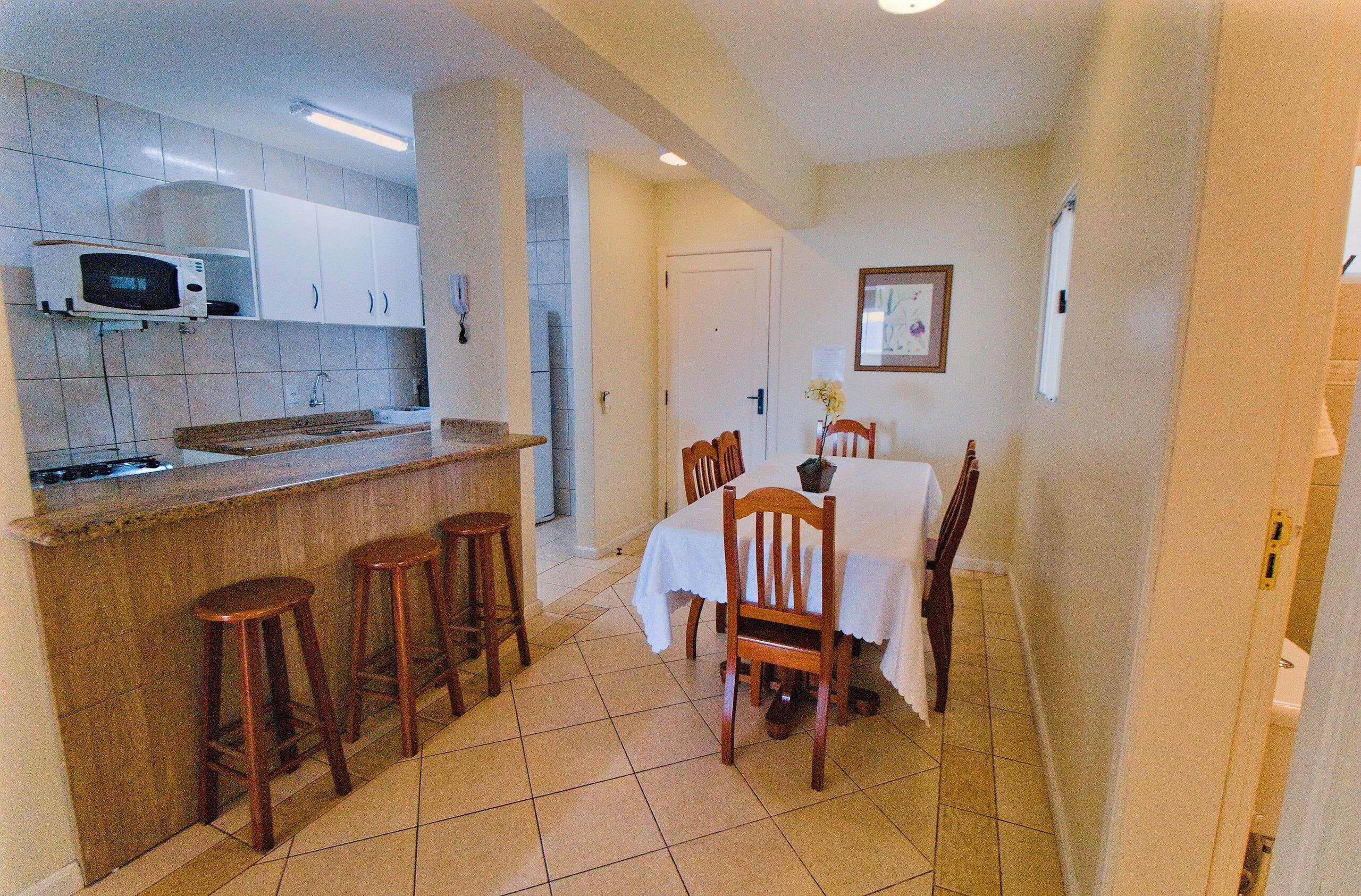 A compact kitchen with a microwave, bar stools, and a dining table with chairs.