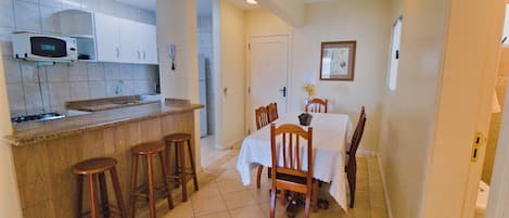 A compact kitchen with a microwave, bar stools, and a dining table with chairs.
