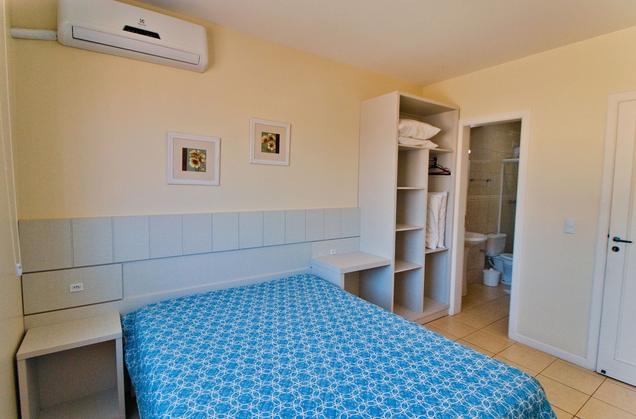 Una camera da letto con un letto, un armadio, un bagno con doccia e due quadri appesi al muro.