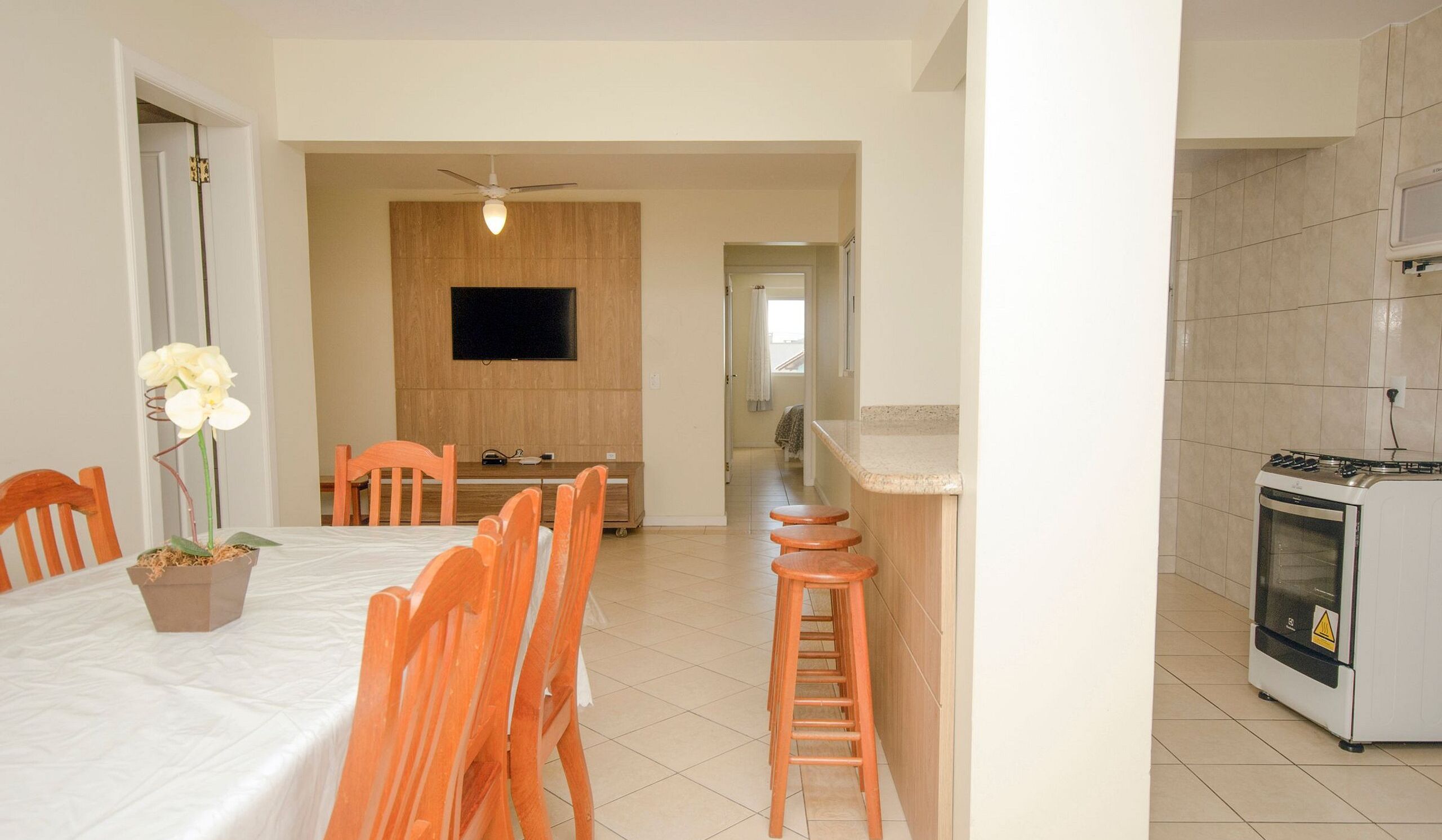Habitación de hotel compacta con comedor, cocina y televisor fijado a la pared.