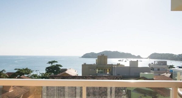 A coastal view from a balcony overlooking a beach with buildings and a distant island. - Residencial Vista Bella (Bombinhas)