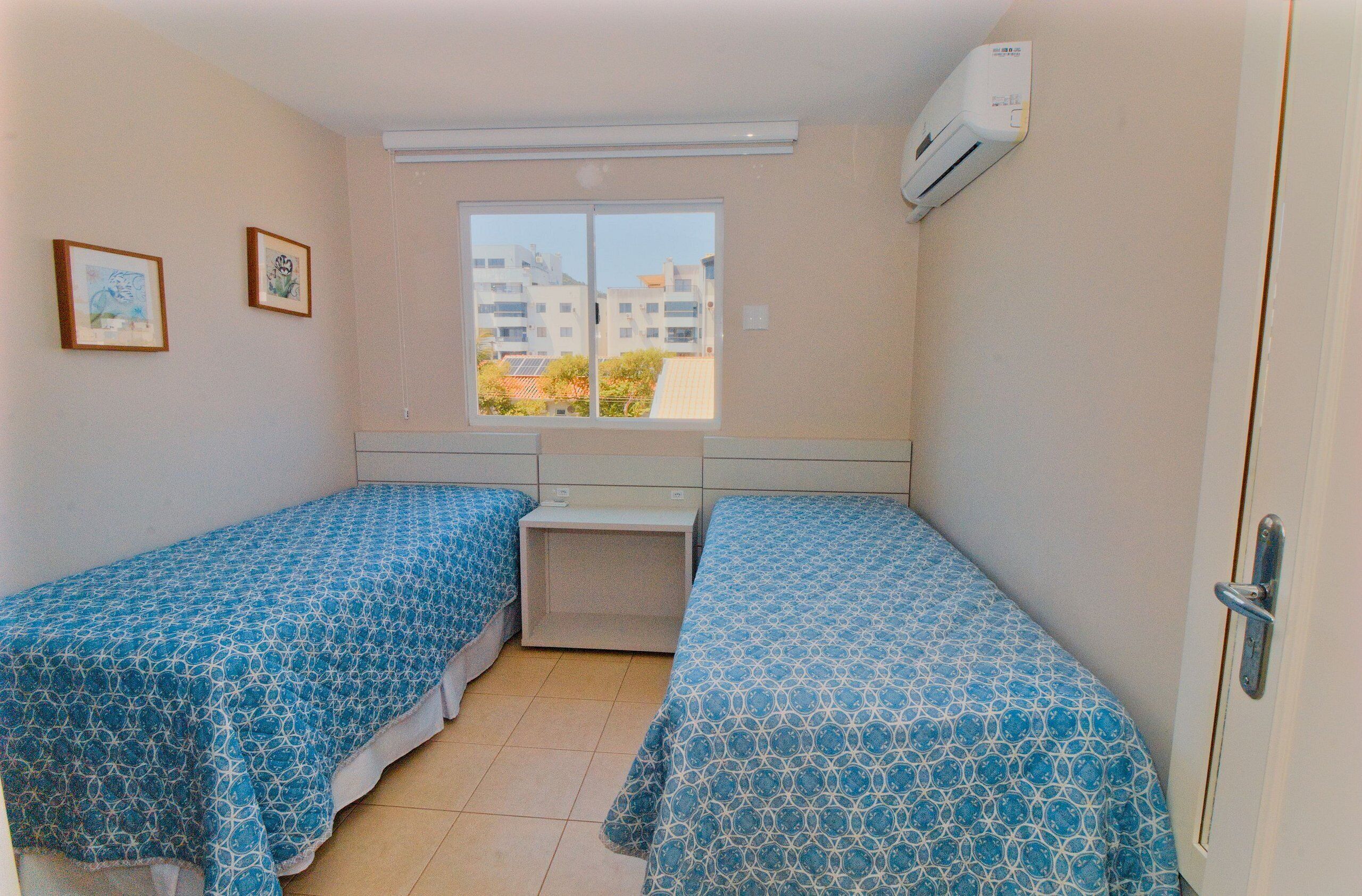 Une petite chambre propre, avec deux lits simples, une fenêtre donnant sur des immeubles et un appareil de climatisation.