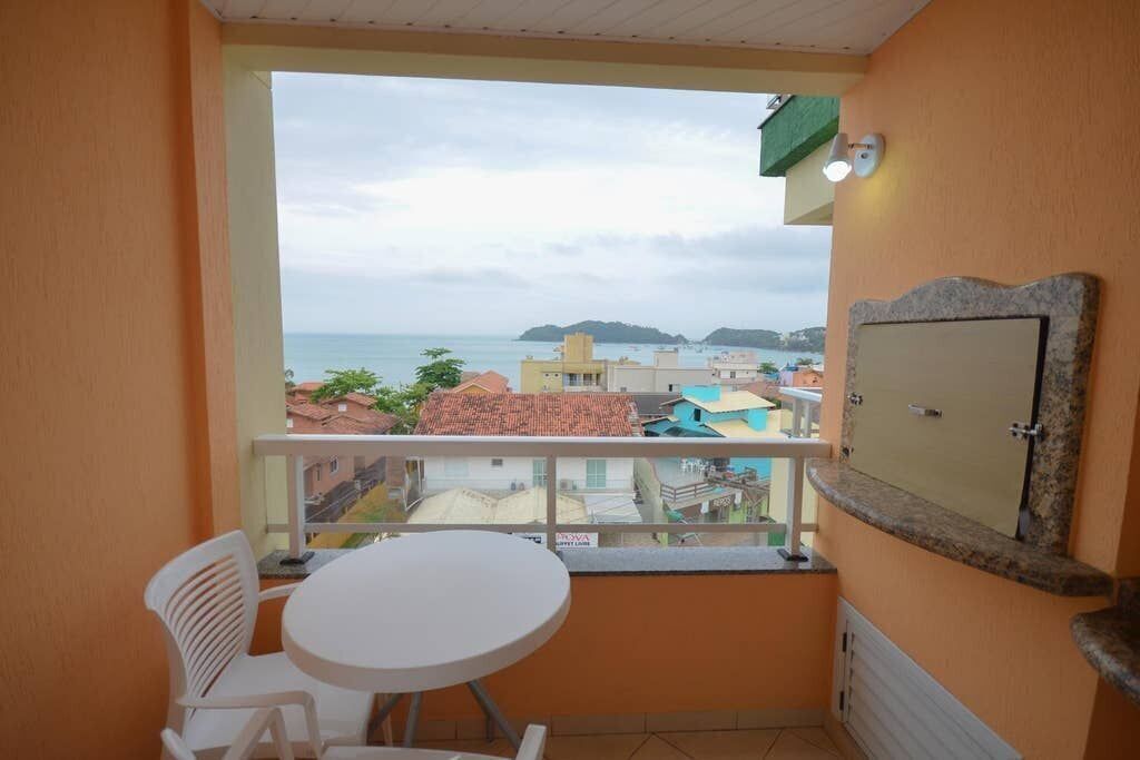 A balcony with a view of the sea, a small table, and a chair.