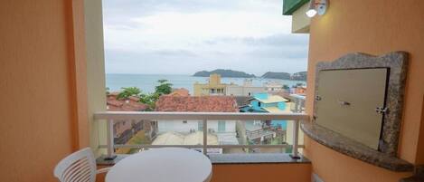 A balcony with a view of the sea, a small table, and a chair.