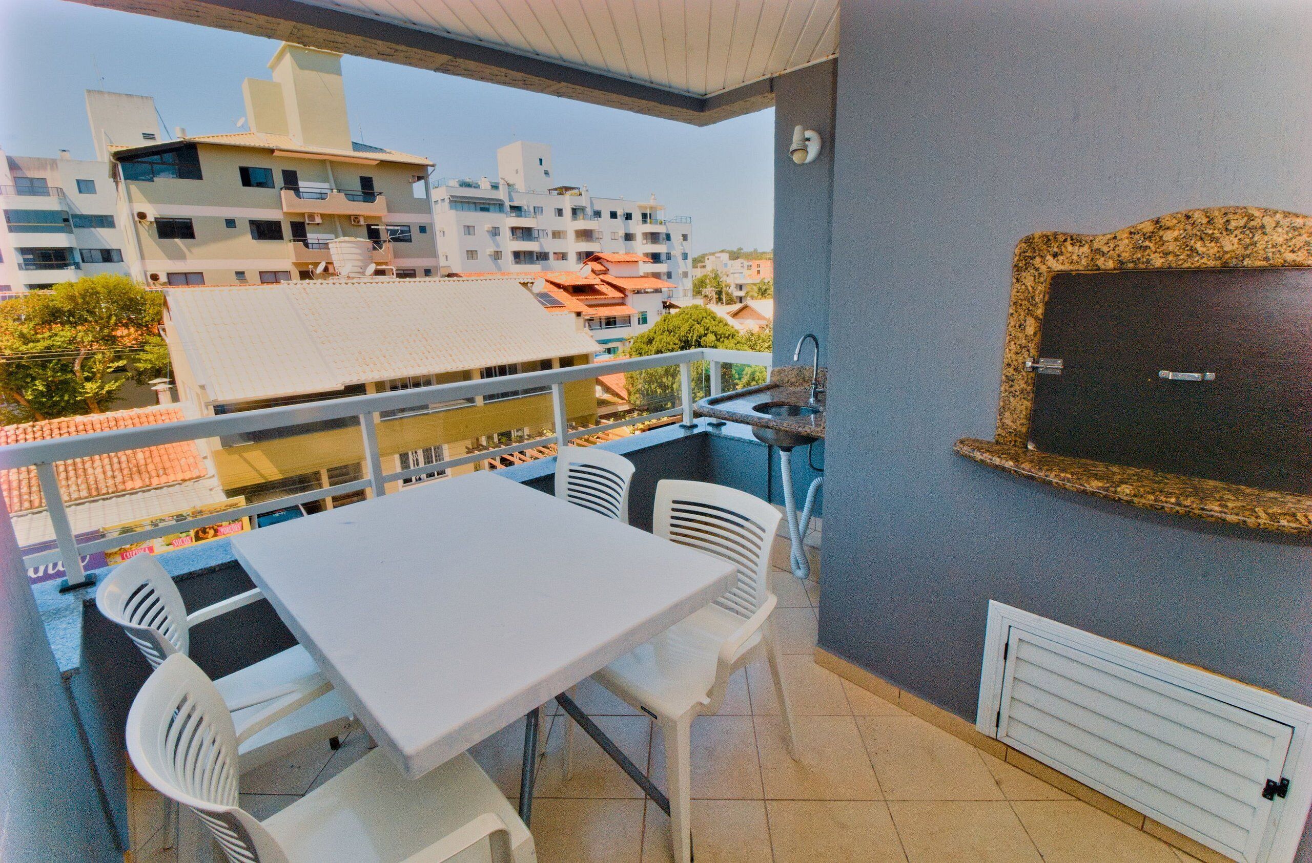 Un balcon avec une table et des chaises blanches, un évier et une vue sur les bâtiments en arrière-plan.
