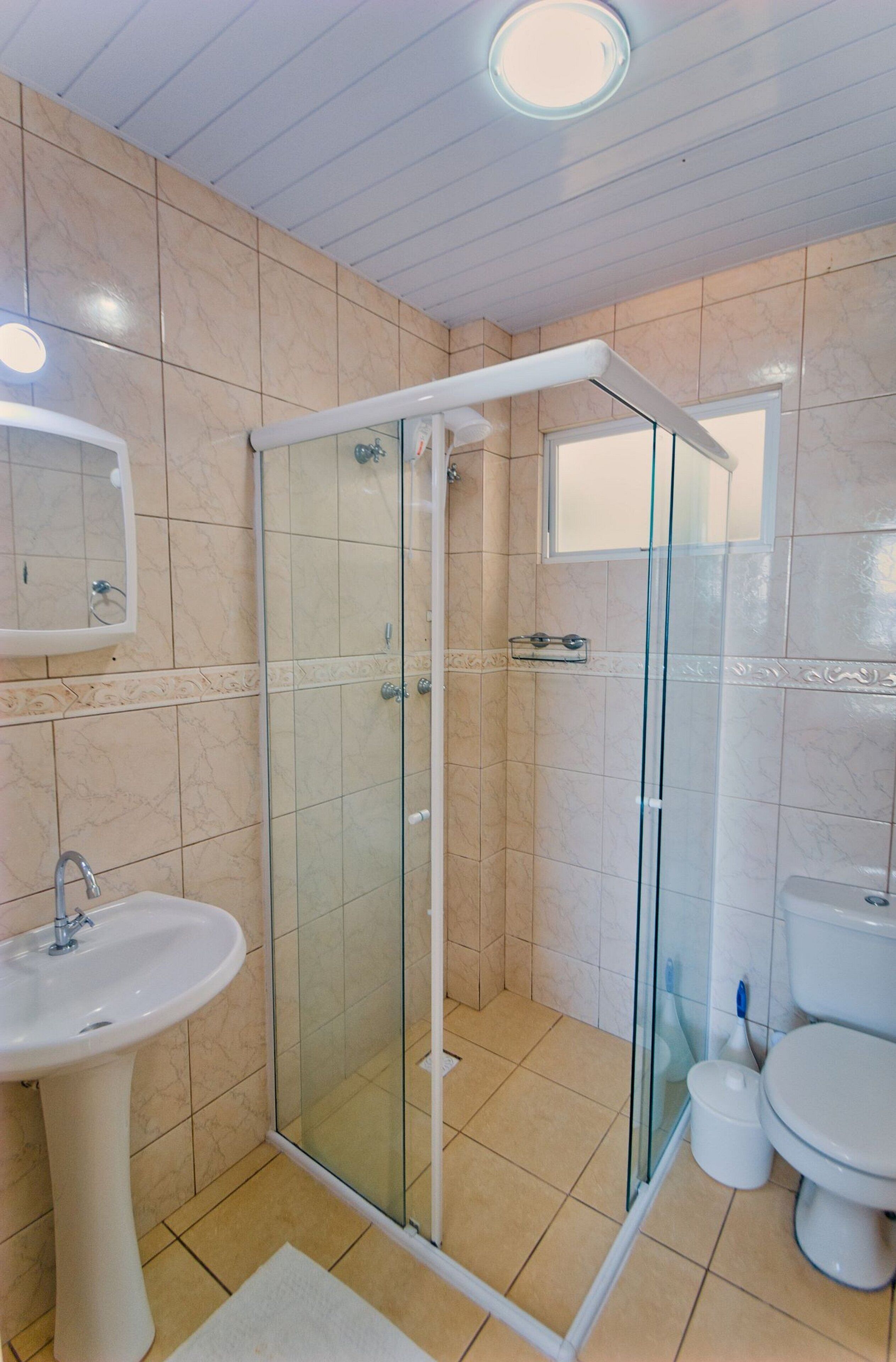 A bathroom with a glass-enclosed shower, a pedestal sink, and a toilet.