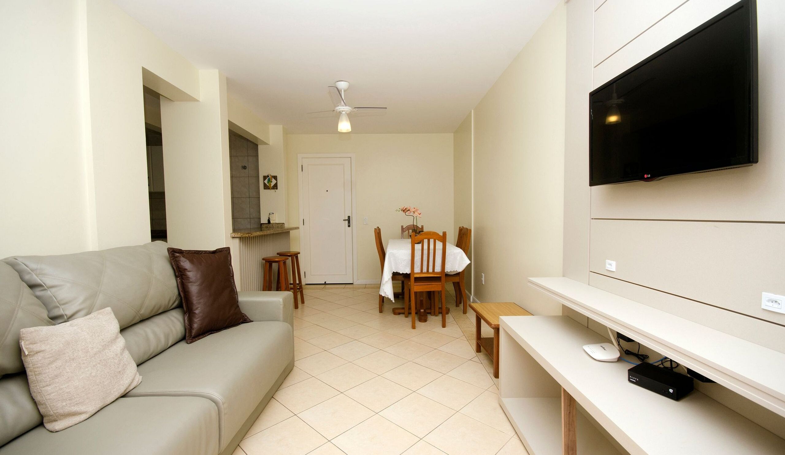 Un espacio habitable compacto con un sofá, una mesa de comedor con sillas, un televisor montado en la pared y un ventilador de techo.