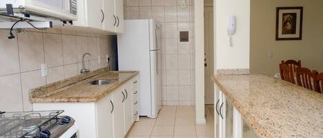 A kitchen with white cabinets, a granite countertop, a stove, a refrigerator, and a microwave.