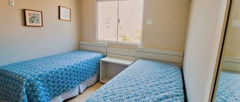 A room with two beds, a window, and two framed pictures on the wall.