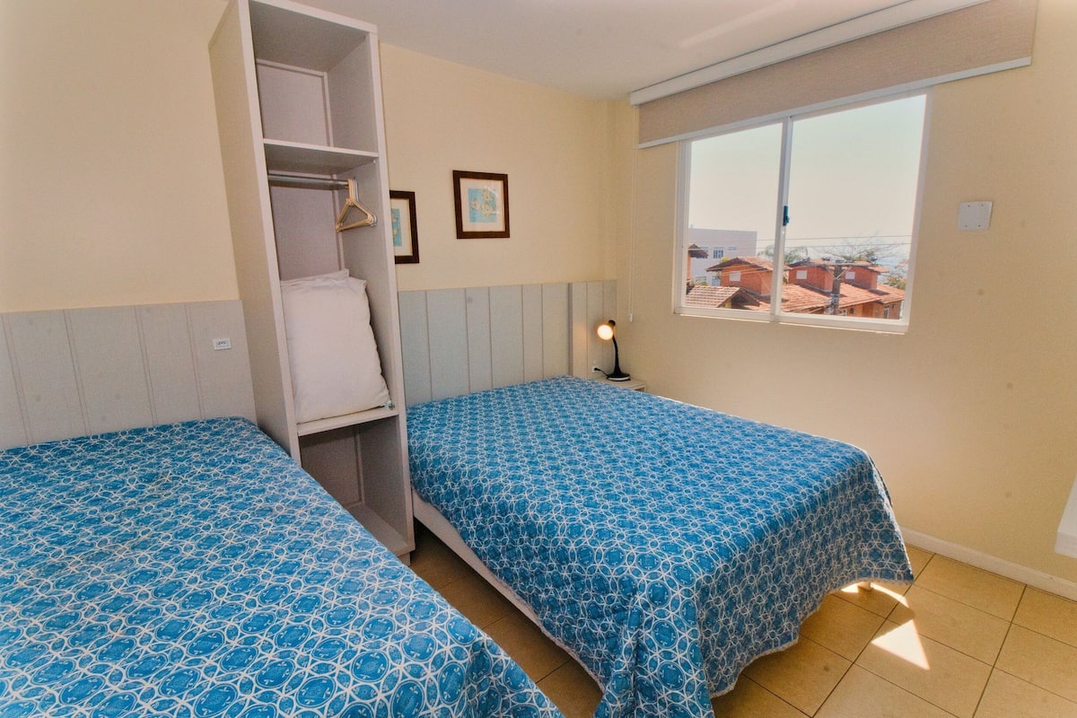 A bedroom with two beds, a wardrobe, a window with a view, and a bedside lamp.