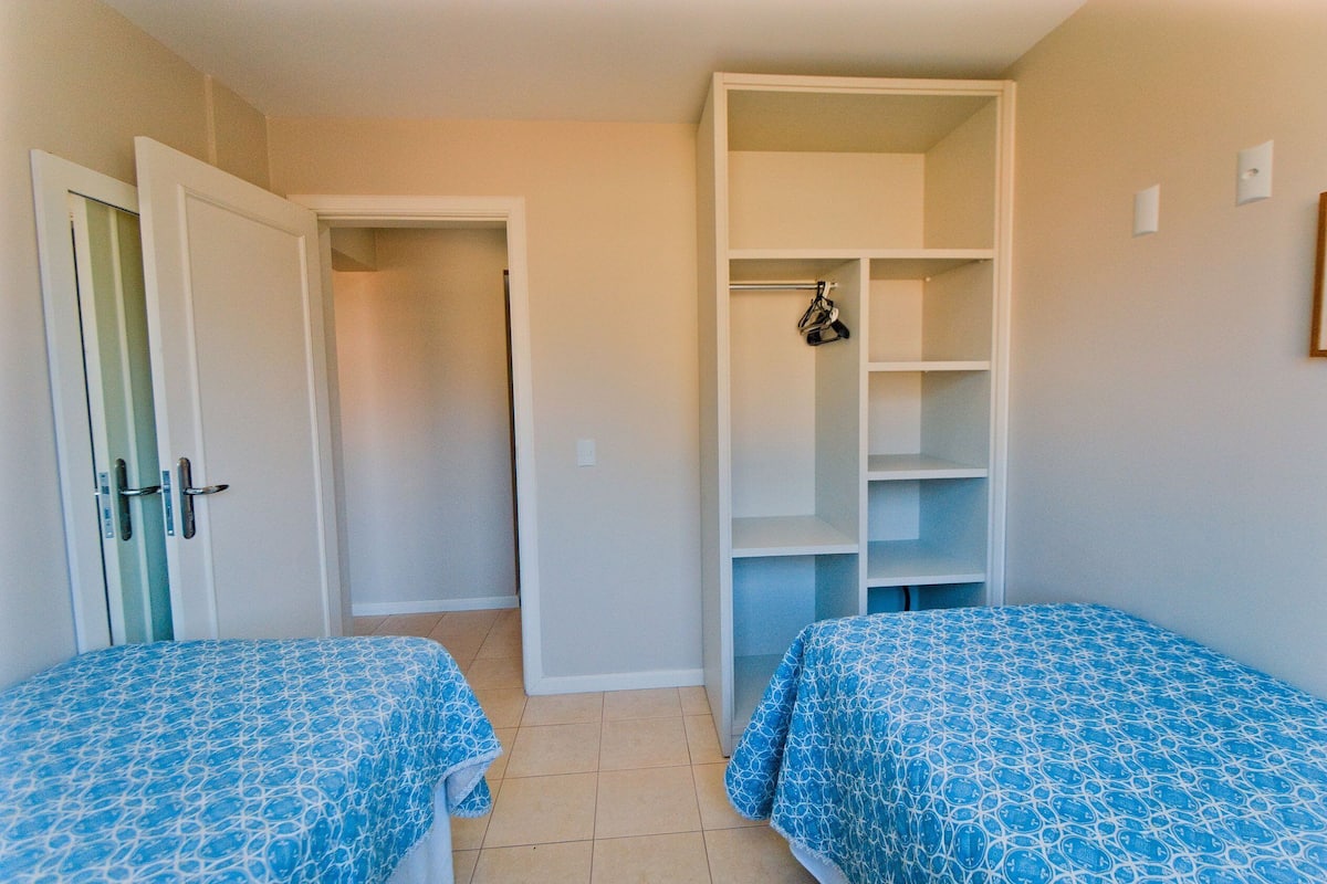 A bedroom with two beds, a wardrobe, and a door leading to another room.
