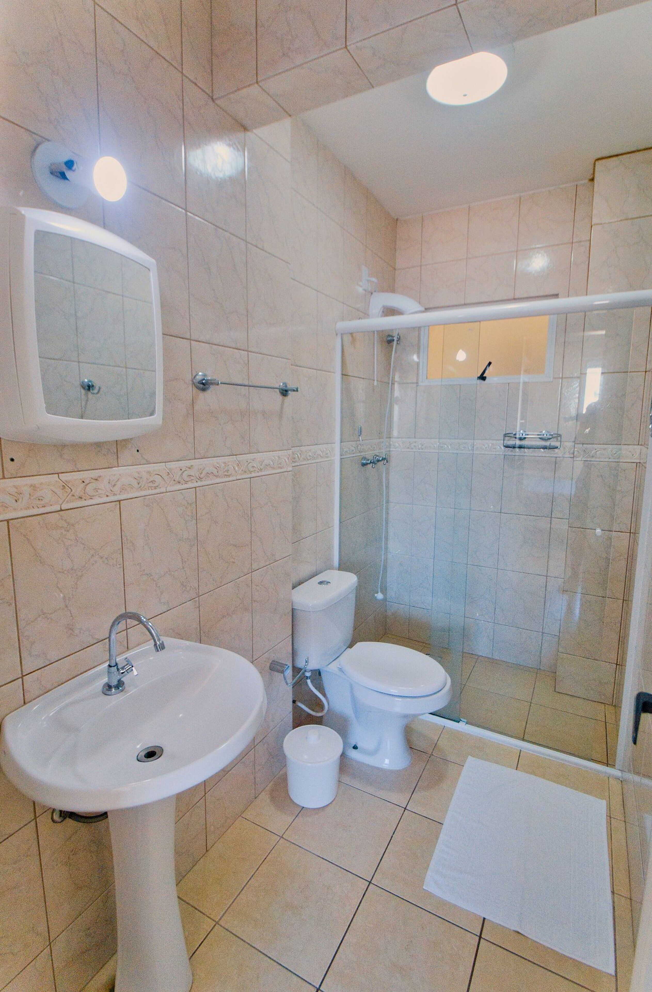 A bathroom with a pedestal sink, two toilets, a shower enclosure, and a mirror above the sink.