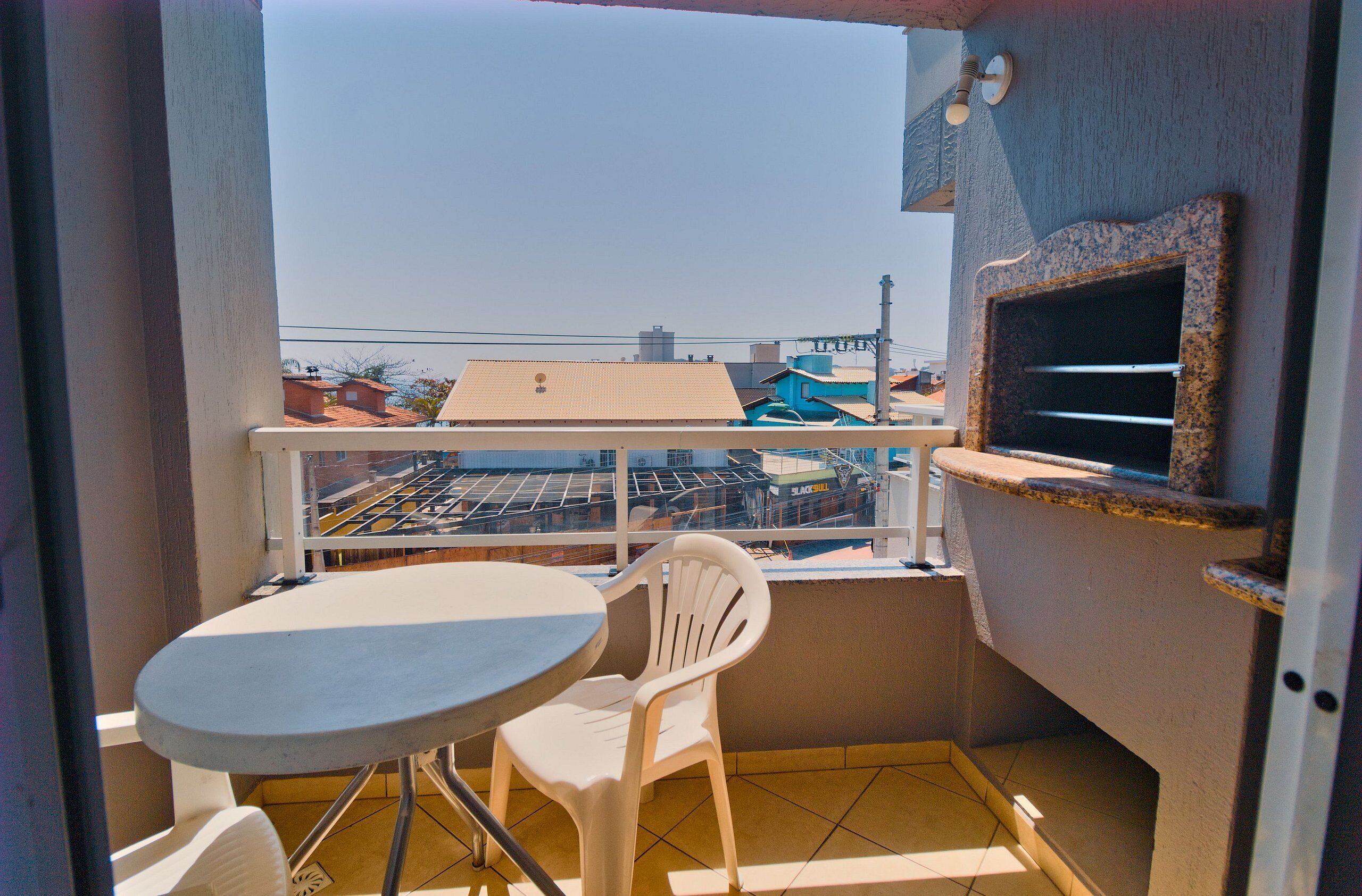 A balcony with a table and a chair, a small sink, and a view of buildings in the distance.
