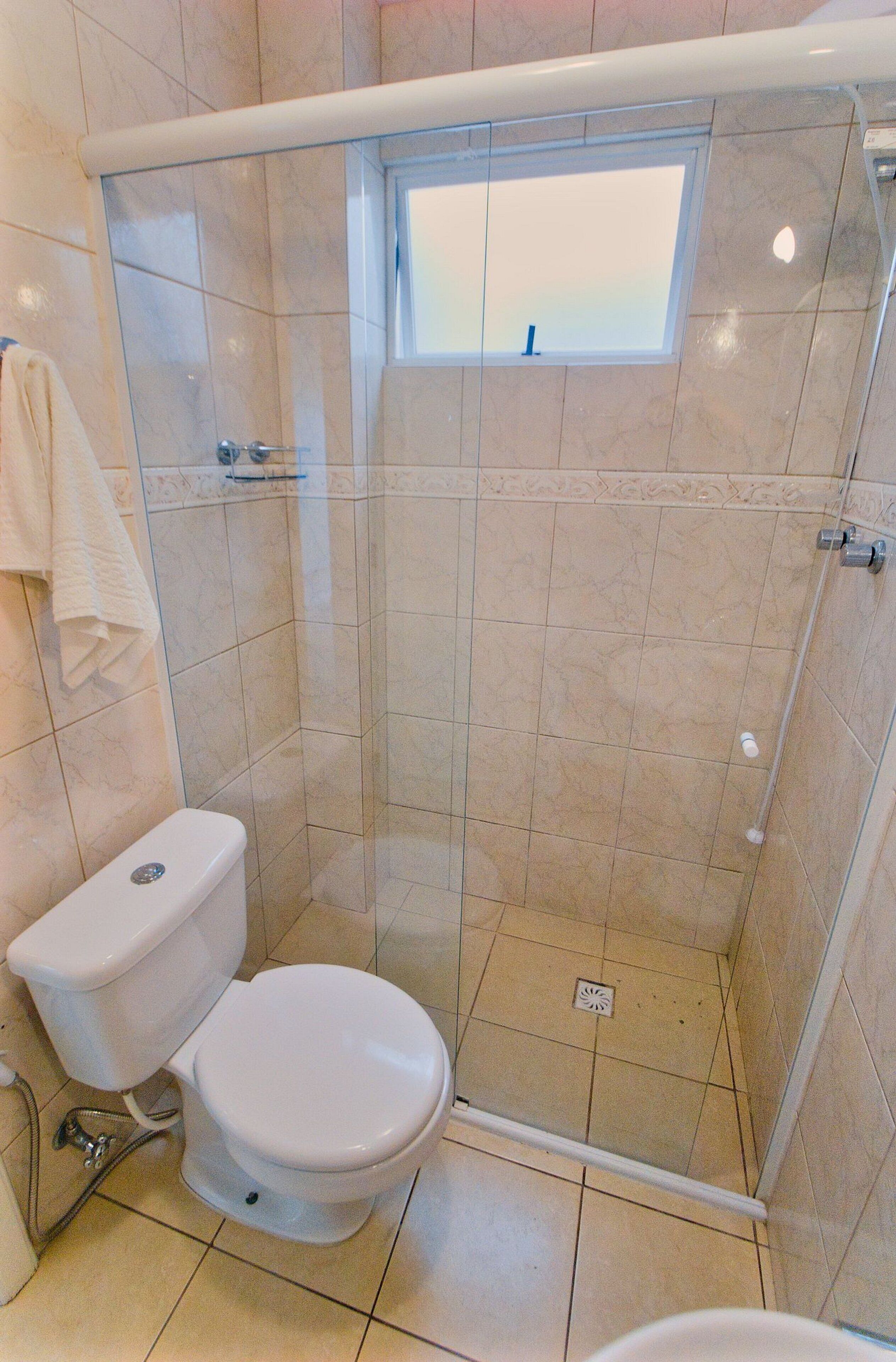 Une salle de bain avec une douche à parois de verre, des toilettes et une petite fenêtre.