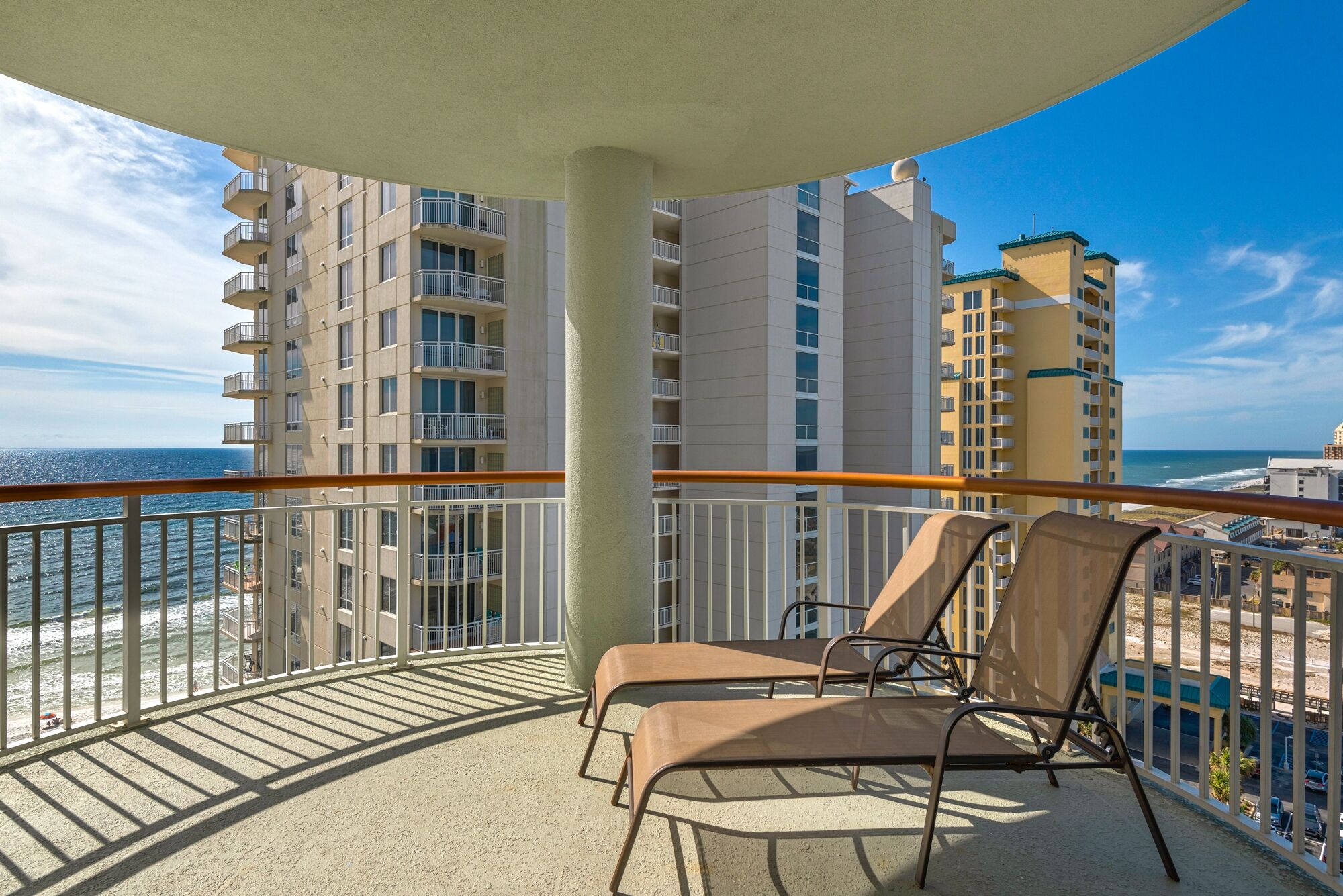 Un balcon avec deux fauteuils de relaxation, une vue sur l’océan et, au loin, des immeubles de grande hauteur.