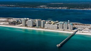 Un hôtel situé sur la côte, composé de plusieurs immeubles de grande hauteur, doté d’une jetée s’avançant dans l’eau et d’une zone de plage.