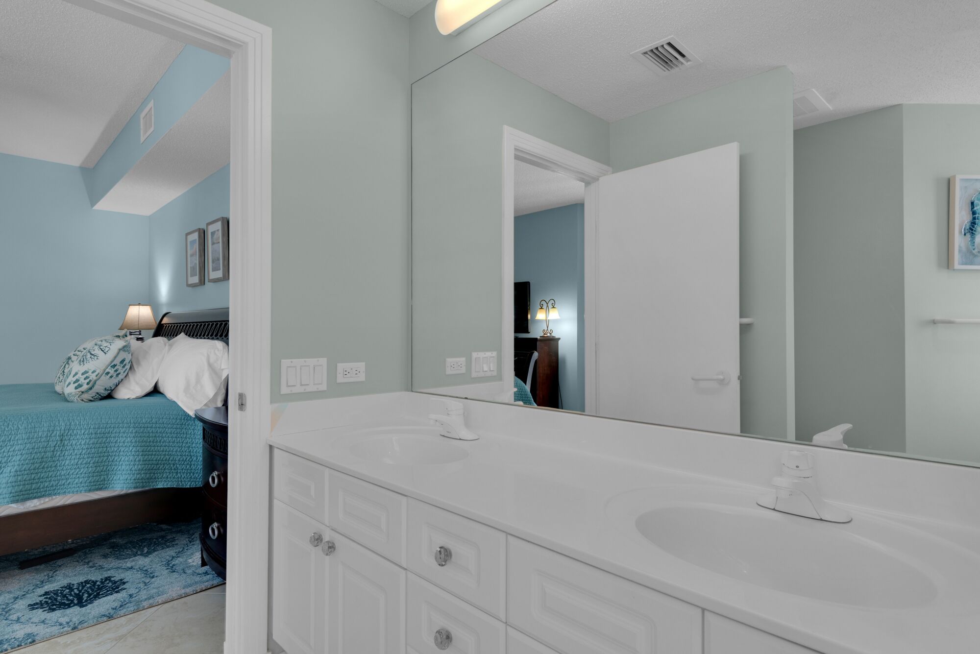 Een slaapkamer met een grote spiegel, een bed met een blauwe dekbedovertrek en een witte dressoir.