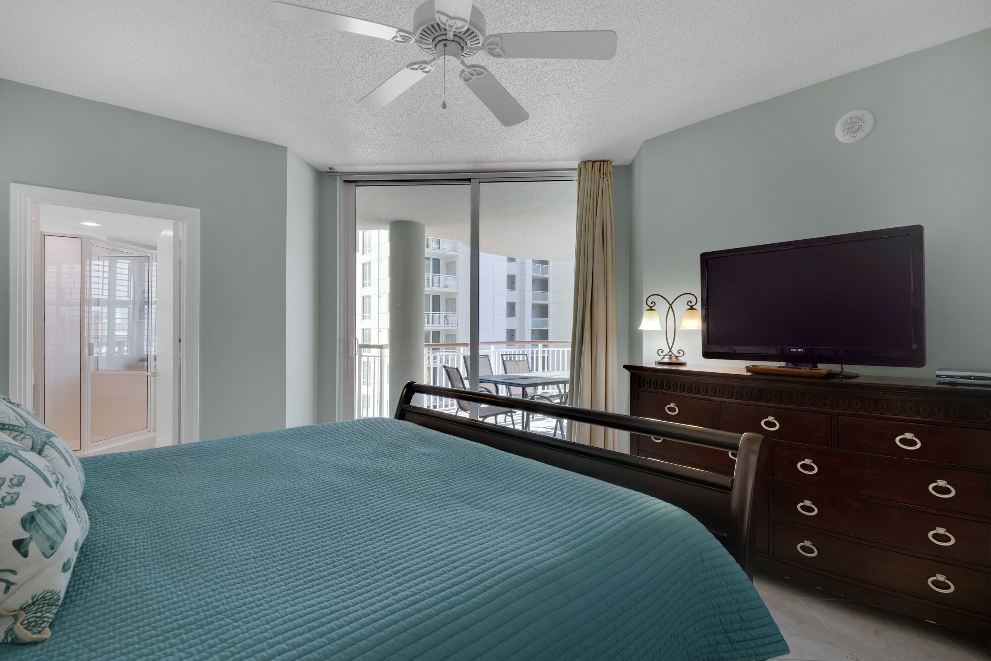 A bedroom with a bed, a television, a dresser, and a balcony with a view of buildings.