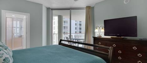 A bedroom with a bed, a television, a dresser, and a balcony with a view of buildings.