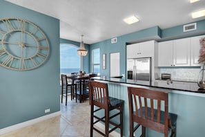 A modern kitchen with a large island, white cabinets, and a view to the outside.